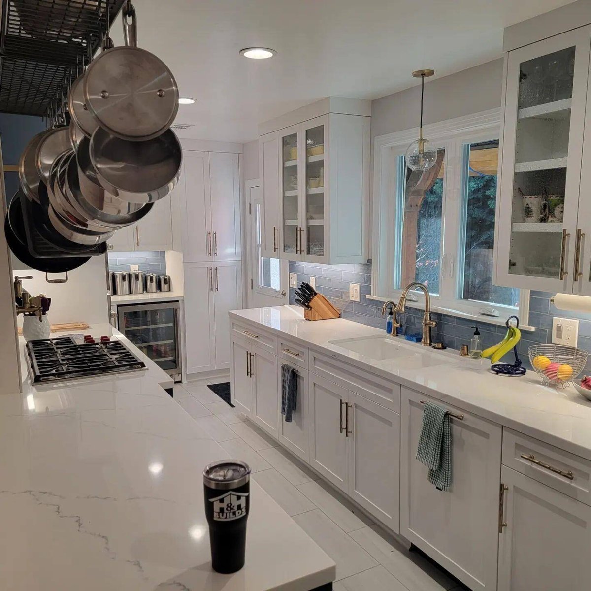 Elegant modern kitchen featuring white cabinetry, hanging pots, and a bright open layout by H&H Builds, Sacramento, CA