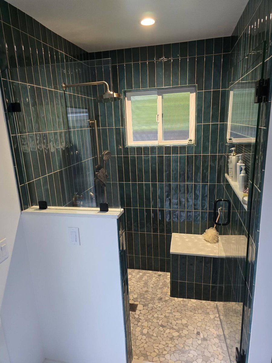 Detailed view of green tiled shower with rainfall showerhead and bench seating in remodel by H&H Builds, Sacramento, CA