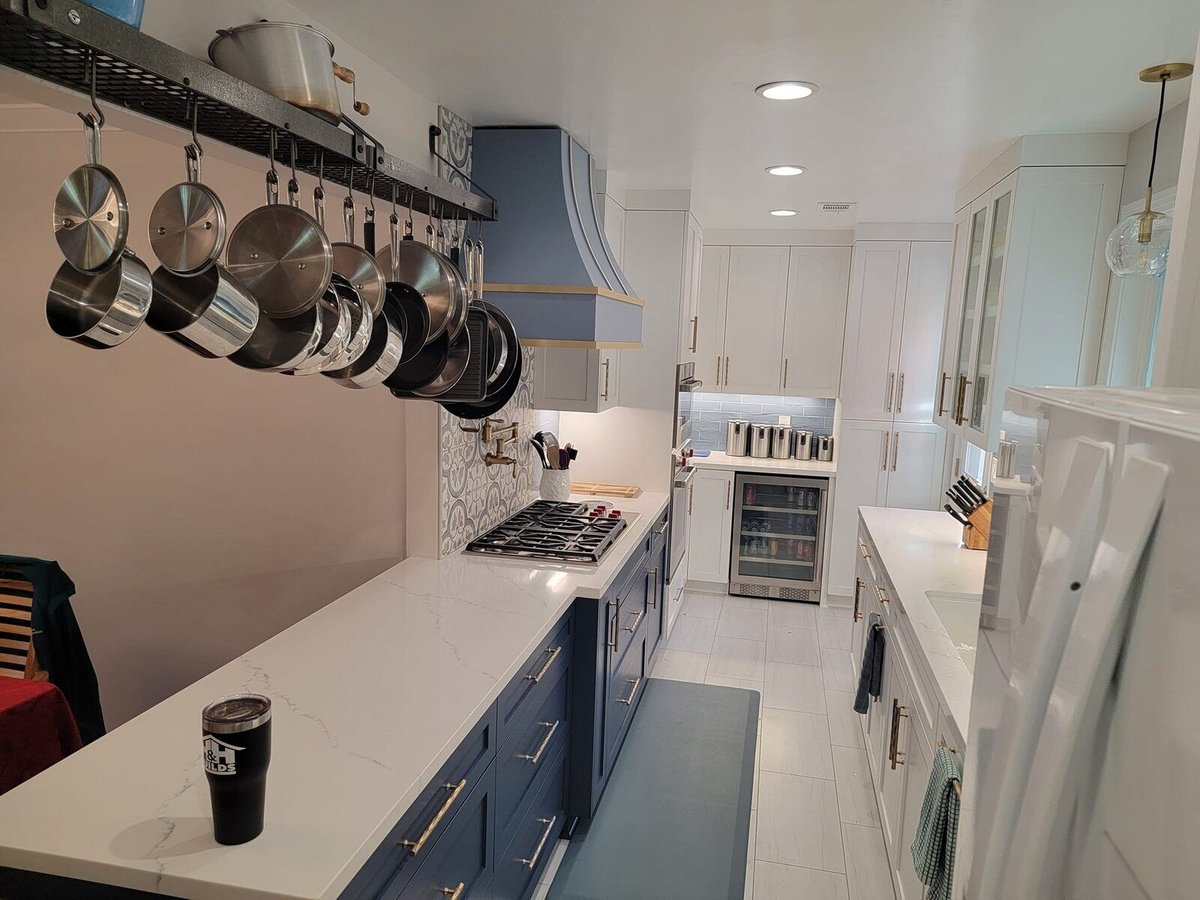 Modern kitchen remodel featuring blue cabinets, white countertops, and hanging stainless steel pots by H&H Builds in Sacramento, CA